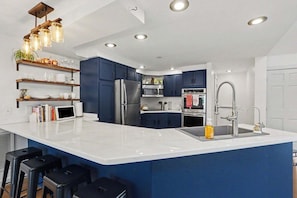 A modern kitchen with a large island, stainless steel appliances, and blue cabinetry.