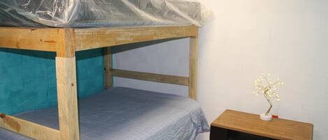 Ein Etagenbett mit einer Matratze und einer Plastikauflage, ein Nachttisch mit einer Lampe sowie eine Wand mit Türkis-Akzent.