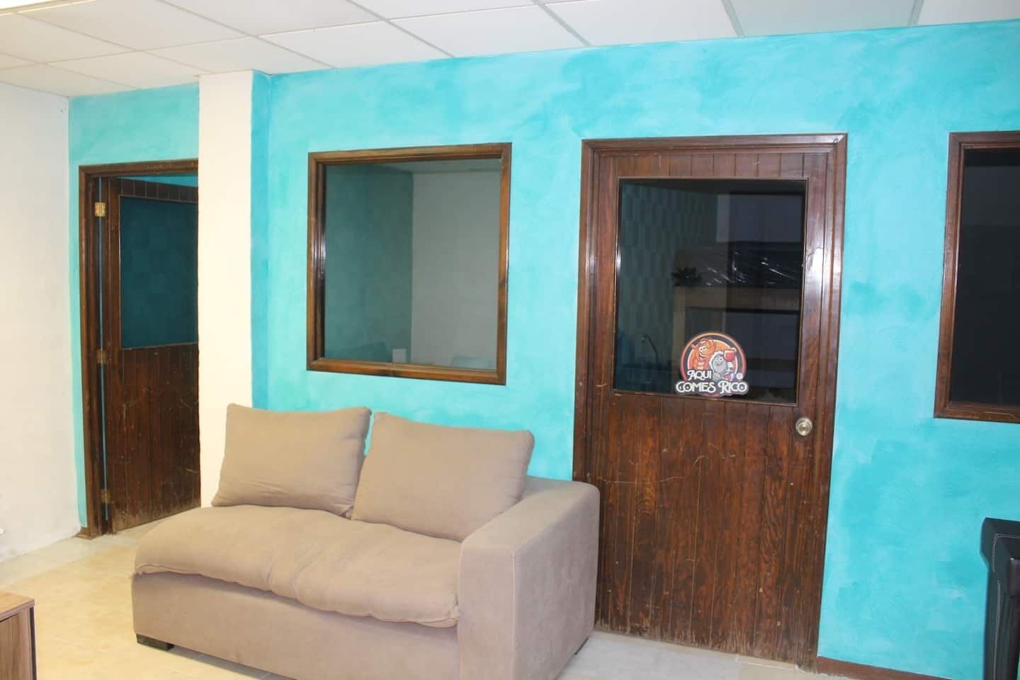 A room with a teal wall, a beige sofa, and two wooden doors with glass panels.