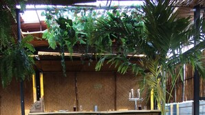 An outdoor seating area with a metal railing, a table with a cushioned bench, and a backdrop of greenery and bamboo.