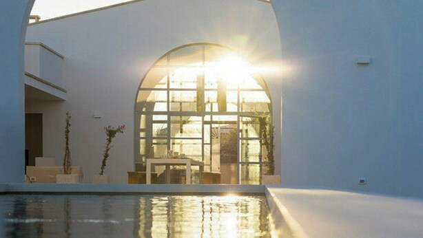 Um edifício moderno com uma grande entrada em arco, uma piscina em primeiro plano e um interior luminoso.