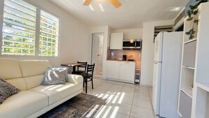 Ein kompakter Wohnraum mit Sofa, Esstisch, Stühlen, einer Küchenzeile mit Geräten und einer integrierten Regaleinrichtung.