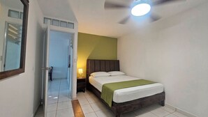Ein Schlafzimmer mit Bett, Nachttisch, Lampe, Deckenventilator und einer Tür zu einem anderen Raum.