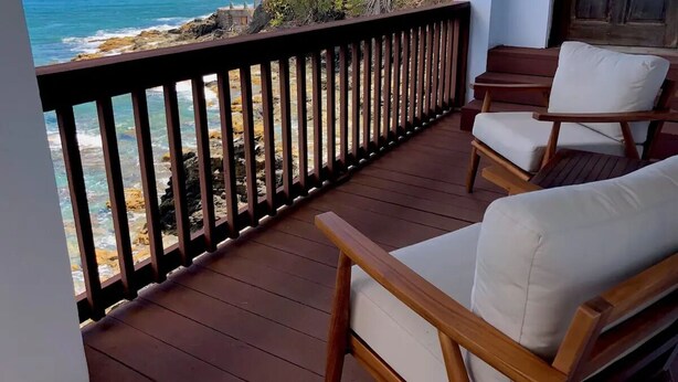 Una terraza de madera con sillas que da a un litoral rocoso y al océano.