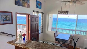 Una cocina con vista al océano, un comedor con mesa y sillas, y una puerta que da al exterior.