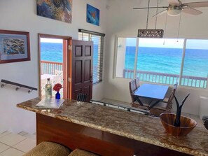 Una cocina con vista al océano, un comedor con mesa y sillas, y una puerta que da al exterior.