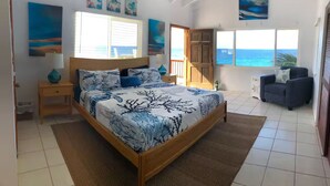 Un dormitorio con cama, mesita de noche, una silla y vistas al océano.