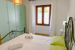 A bedroom with a bed, a window, a wardrobe, and a bedside table. - Appartamento l'Anfora (Cala Gonone)
