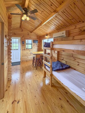 A cabin interior with wooden walls, a bunk bed, a desk, and a ceiling fan.