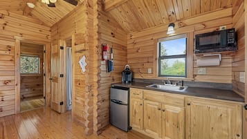 A wooden cabin interior with a kitchen area, including a refrigerator, microwave, and sink.