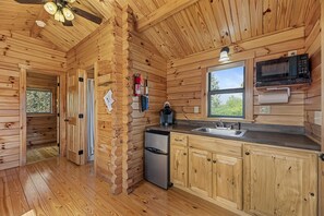 A wooden cabin interior with a kitchen area, including a refrigerator, microwave, and sink.