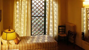 Ein Zimmer mit einem Bett, einem Sessel, einem Tisch mit Handtüchern, einer Lampe und einem Fenster mit Vorhängen.