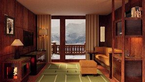 Una habitación con interior de madera, chimenea, sofá, mesa, estantería y vistas a las montañas a través de un ventanal grande.