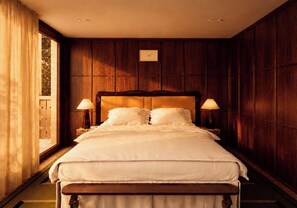Un cuarto de hotel con una cama grande, paneles de madera en las paredes, un ventanal con cortinas y dos lámparas de noche.