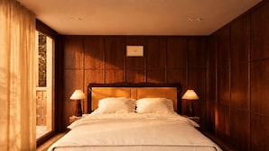 Habitación de hotel con una cama grande, paneles de madera, dos lámparas de noche y un ventanal con cortinas.