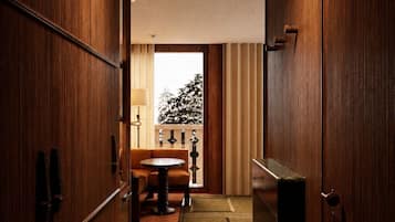 A narrow hallway with wooden paneling, a small table with chairs, and a view of a balcony with curtains.