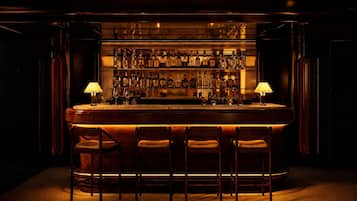A bar with a wooden counter, multiple liquor bottles, and four bar stools.