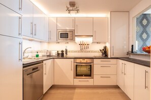 Een moderne keuken met witte kasten, roestvrijstalen apparatuur en een houten vloer.