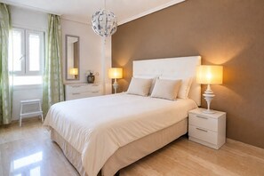 Een slaapkamer met een groot bed, twee nachtkastjes met lampen, een kaptafel, een spiegel en een raam met gordijnen.