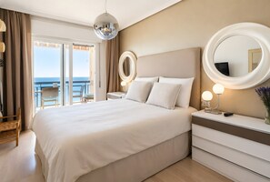 Et hotelværelse med en stor seng, et natbord med et spejl, en kommode og en balkon med havudsigt.
