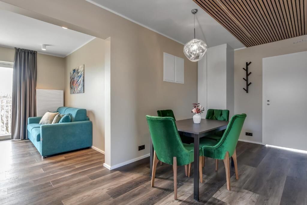 En moderne stue med en turkis sofa, grønne lænestole, et spisebord og en pendel.