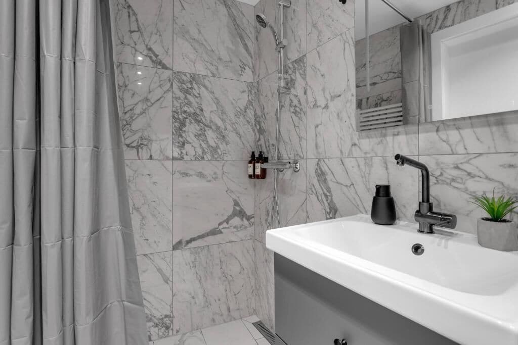 A bathroom with a shower, a sink, a mirror, and a plant.