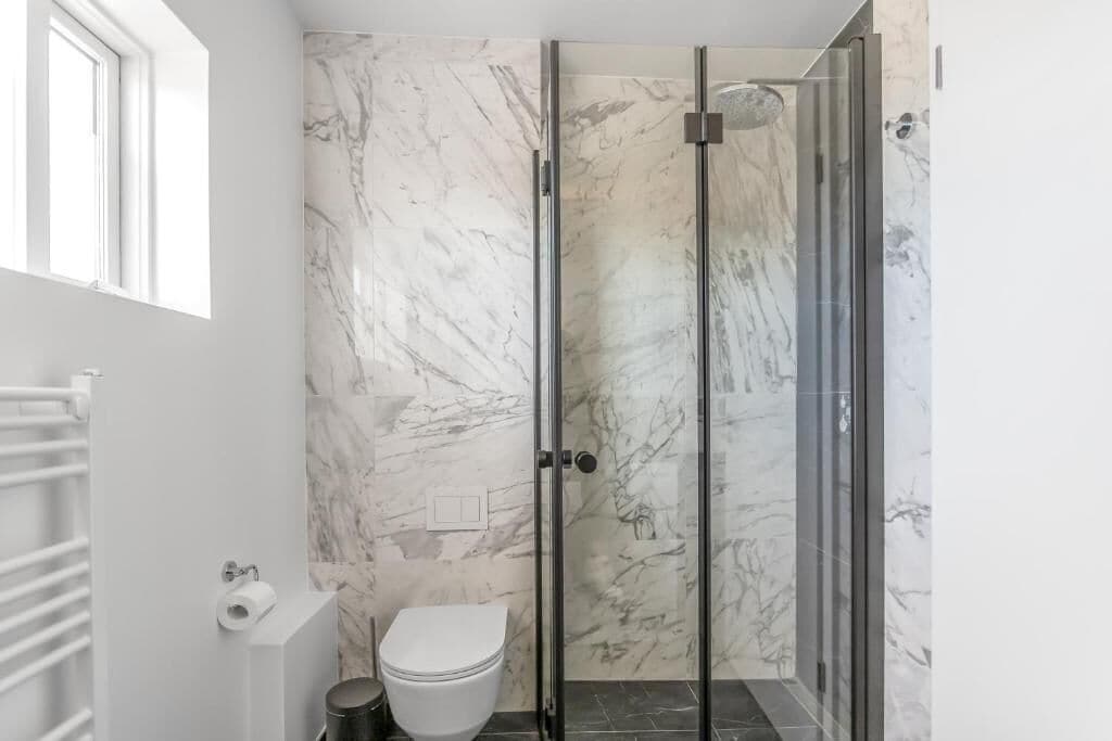 A bathroom with a toilet, a shower with glass doors, and a marble wall.