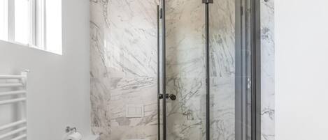 A bathroom with a toilet, a shower with glass doors, and a marble wall.