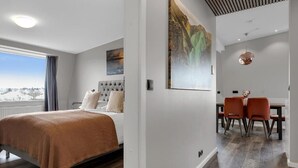 Moderni hotellihuone, jossa on suuri sänky, ruokailutila tuoleineen ja näkymä ikkunasta.