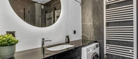 Un baño moderno con un espejo redondo, un lavabo, una lavadora y un perchero para toallas.