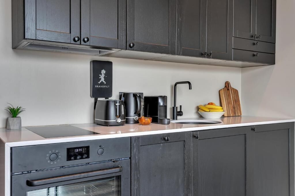 A modern kitchen with grey cabinets, a built-in oven, a coffee maker, a kettle, and a fruit bowl.