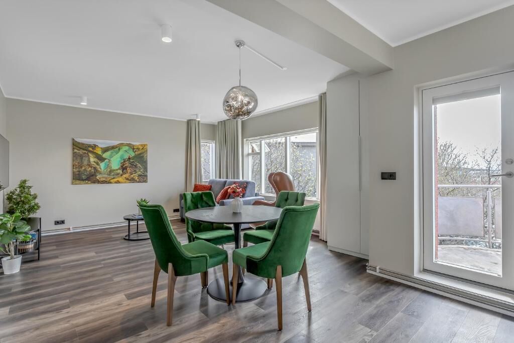 A modern dining area with a round table, green chairs, and a large window.