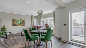 A modern dining area with a round table, green chairs, and a large window.