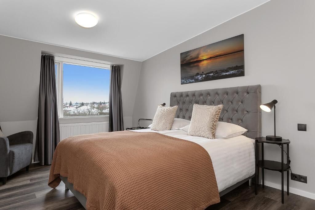 Ein Schlafzimmer mit einem großen Bett, Blick auf die Stadt, einem Sessel und einem Nachttisch mit Lampe.