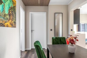A dining area with a dark table, green upholstered chairs, a vase with flowers, a white door, and a large mirror on the wall. - ALVA Apartments Snorrabraut (Reykjavík)