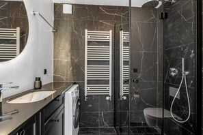 A modern bathroom with a marble backsplash, a built-in sink, a toilet, a shower enclosure, and a towel rack. - ALVA Apartments Snorrabraut (Reykjavík)