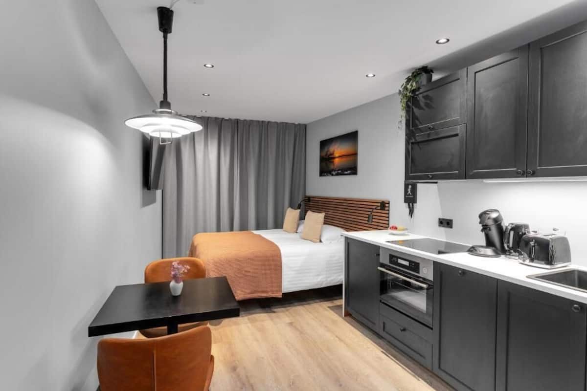 Quarto de hotel compacto com uma cama, uma pequena mesa de jantar, uma cozinha compacta e uma luminária no teto.
