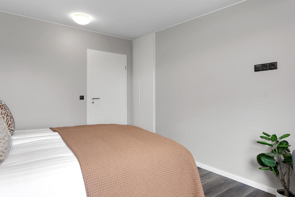 A bedroom with a bed, a door, a wall-mounted light, and a potted plant.