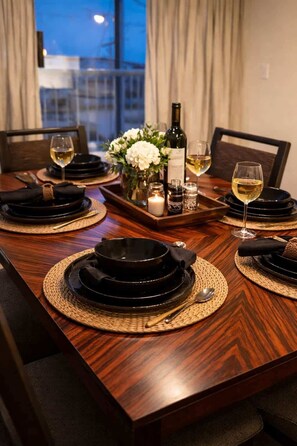 A dining table set with black plates, a bottle of wine, glasses, and a candle. - Cozy 2 BR-5min Downtown • Walk to Shops & Transit (Vancouver)
