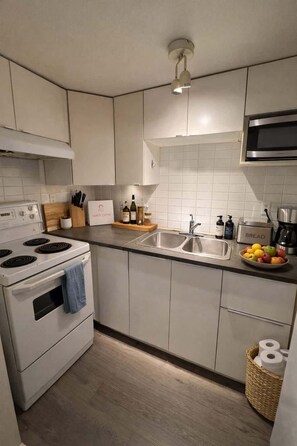 A modern kitchen with a stove, sink, and microwave. - Cozy 2 BR-5min Downtown • Walk to Shops & Transit (Vancouver)