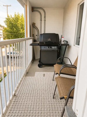 A balcony with a grill, chairs, and a view of the street. - Cozy 2 BR-5min Downtown • Walk to Shops & Transit (Vancouver)