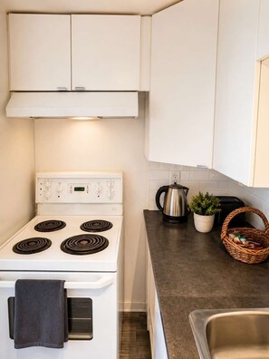 A kitchen with a white stove, a kettle, a potted plant, and a basket on the counter.