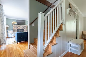 Eine Treppe mit weißen Geländern und Holzstufen, ein blaues Sofa, ein Steinkamin und ein kleiner weißer Tisch.