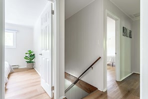 Ein Flur mit Holzboden, weißen Wänden und einer Treppe mit hölzernem Geländer.