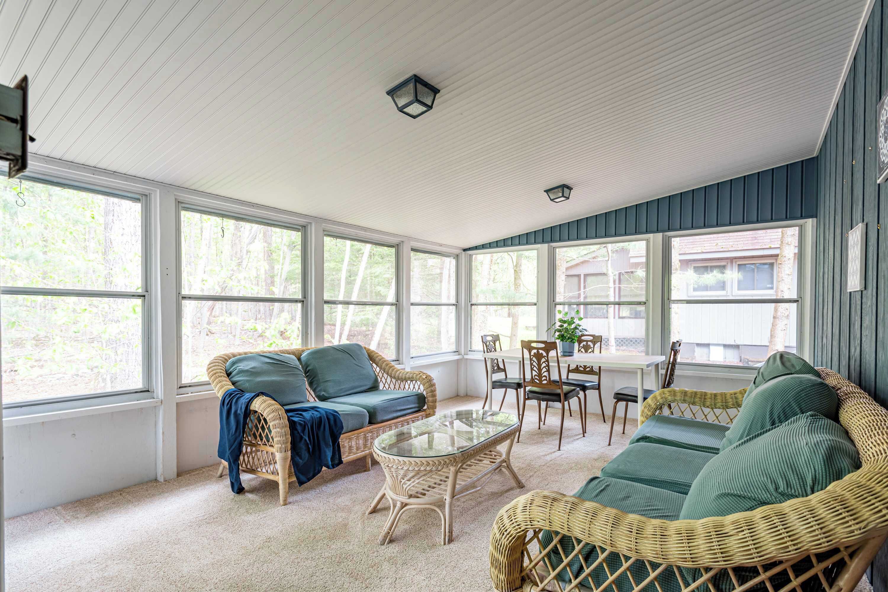 A sunroom with wicker furniture, large windows, and a ceiling fan.