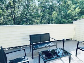 Un patio con un banco y una mesa, rodeado por una valla blanca y árboles.