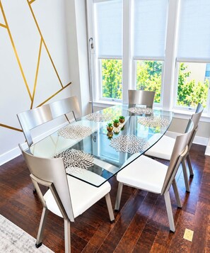 A modern dining area with a glass table, white chairs, and a view of greenery outside. - Gorgeous 4-Level House with Private Parking in Serene Washington Neighborhood (Washington)