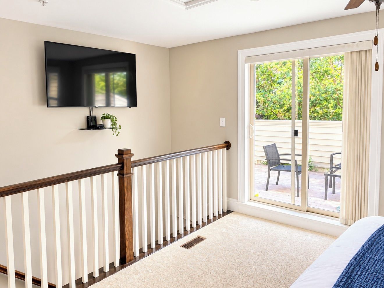 A bedroom with a large window, a flat-screen TV mounted on the wall, and a wooden railing.