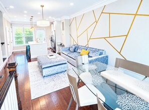 A modern living room with a glass dining table, blue patterned sofas, and a geometric wall design. - Gorgeous 4-Level House with Private Parking in Serene Washington Neighborhood (Washington)