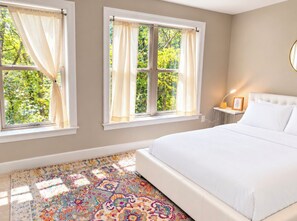 A bedroom with a large bed, two windows with curtains, a bedside table with a lamp, and a patterned rug. - Gorgeous 4-Level House with Private Parking in Serene Washington Neighborhood (Washington)